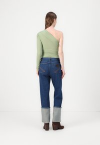 Asimetrična bluza na eni rami svetlo zelene barve, v kombinaciji z modrimi kavbojkami z svetlo sivimi manšetami in temno rjavimi gležnjarji.