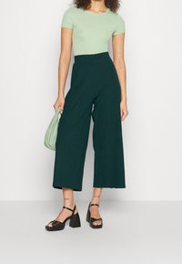 Zielona, prążkowana koszulka, szerokie, ciemnozielone spodnie, czarne, masywne obcasy i mała, jasnozielona torebka. Proste, czyste linie, bez wzorów.