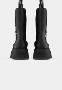 Bottes à plateforme noires avec "KARL" embossé sur le talon et des tirants en tissu avec un texte logo blanc au dos.
