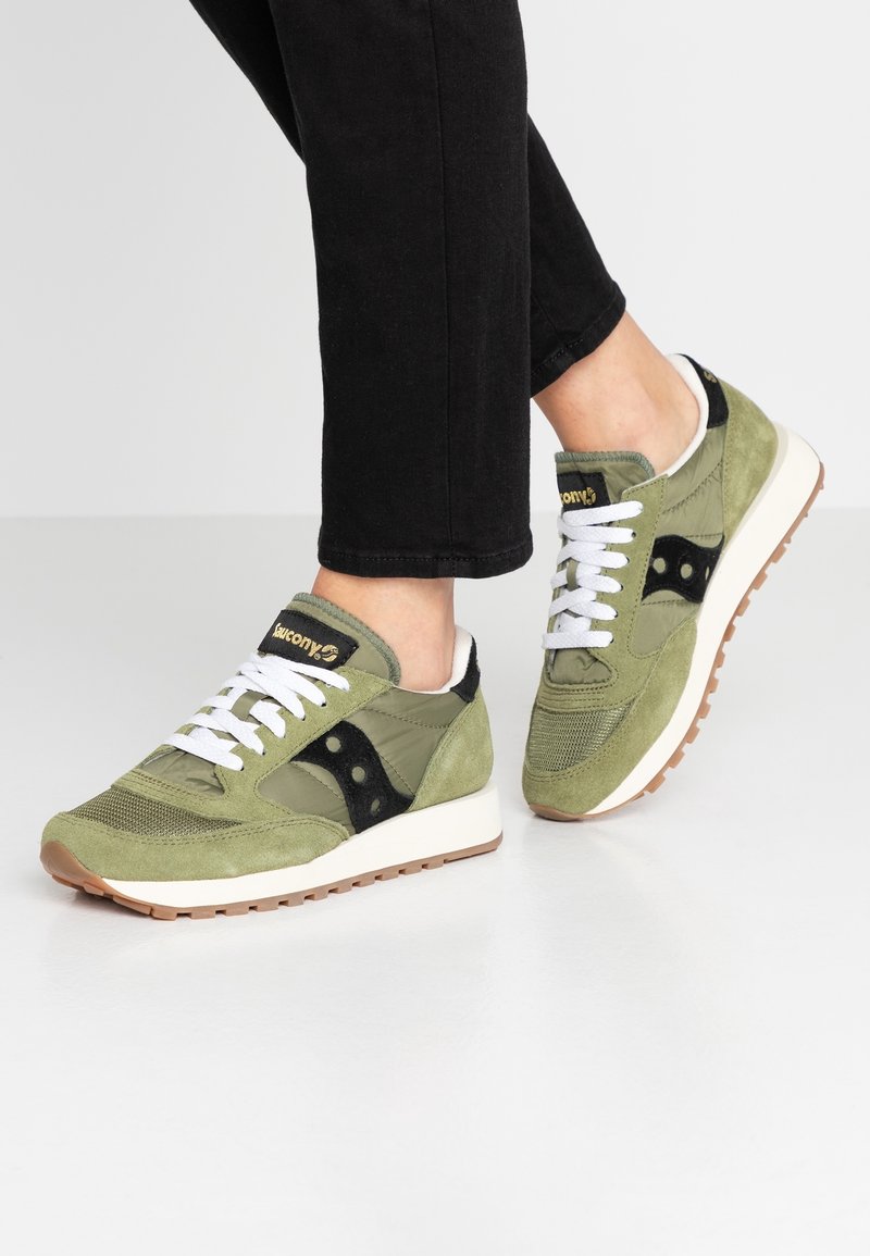 Vihreät mokkanahkakengät, joissa on verkkokärki, mustat yksityiskohdat, valkoiset nauhat ja beige pohja. Kengissä on logo kielessä ja sivussa.