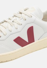 Hvite lær sneakers med teksturert overflate, når burgunder "V"-logo, kremfargede snører og en beige gummisåle.