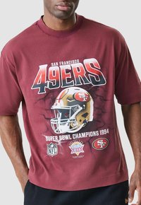 Bordeauxrotes T-Shirt mit einem grafischen Aufdruck eines San Francisco 49ers Helms, dem Logo der Super Bowl Champions 1994 und NFL-Symbolen. Kurze Ärmel, lockere Passform.