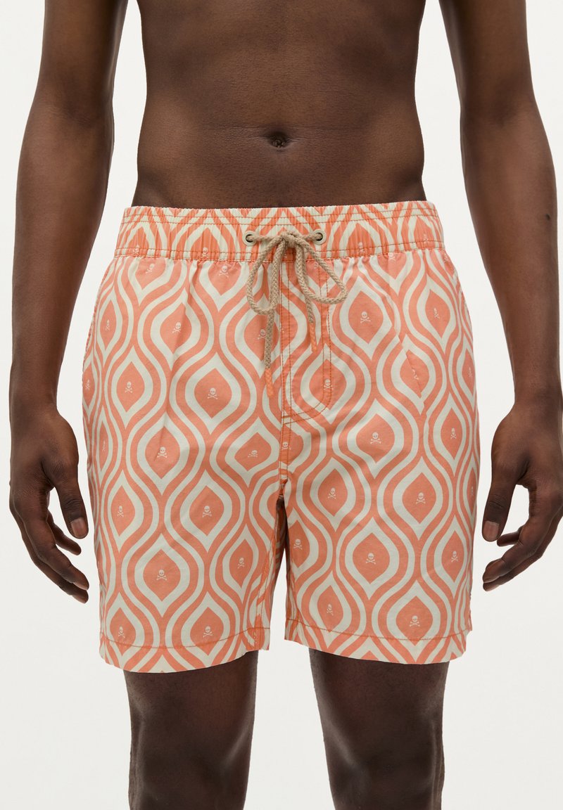 Shorts de bain à motifs présentant un design de vagues pêche et crème avec de petits accents de crânes, taille élastique et fermeture à cordon.