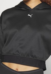 Hoodie nero cropped realizzato in materiale liscio, con tasca frontale a marsupio, orlo a costine e logo Puma bianco sul petto.