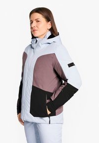 Giacca impermeabile blu chiaro e viola con una sezione inferiore nera, tasche con zip e cappuccio. Texture liscia e design a blocchi di colore.