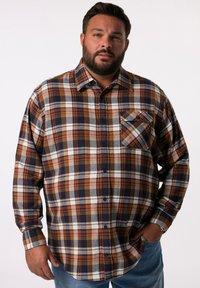 Camicia di flanella in pattern a quadri blu navy, marrone e crema con chiusura a bottoni e una tasca sul petto. Maniche lunghe con polsini a bottoni.