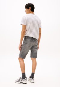 Grå denimshorts med rett snitt, kombinert med en lys stripete t-skjorte. Sneakers med et design i hvitt og svart fullfører antrekket.