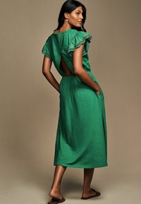 Vestito maxi verde con maniche corte arricciate, dettaglio della schiena scoperta, vita elastica e tasche laterali, realizzato in un tessuto testurizzato.