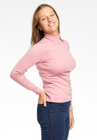 Maglia a maniche lunghe rosa a collo alto con un design aderente e una texture liscia, abbinata a jeans scuri con un accento laterale di paillettes.