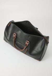 Bolsa de viaje de piel negra con asas de cuero marrón, bolsillo frontal con cremallera y textura suave. Parte superior abierta para un fácil acceso al interior.