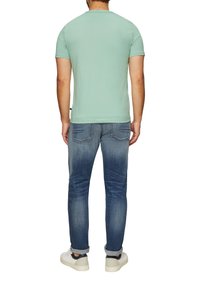 Lichtgroene katoenen t-shirt met een ronde hals, gecombineerd met vervaagde blauwe denim jeans. De outfit wordt compleet gemaakt met witte sneakers.