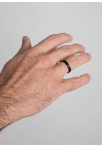 Black metal ring with a geometric design, shown on a hand. The surface is smooth with a matte finish, set against a neutral background.