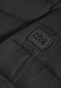 Svart puffjacka med kviltad textur och en rektangulär broderad patch märkt "POLO CLUB". Slät, vattenavvisande tyg.