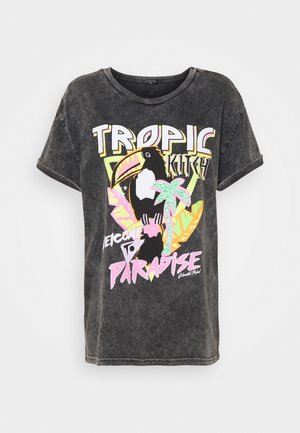 Camiseta gráfica en negro, con un tucán colorido y motivos tropicales. El diseño incluye el texto "TROPIC KITCH" y "WELCOME TO PARADISE."