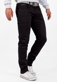 Zwarte denim jeans met een slim fit, vijf zakken, subtiele merkembleem op de tailleband en gestikt detail. Vergezeld van witte sneakers.