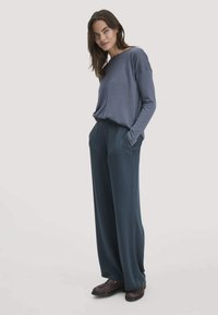 Lässiges, weit geschnittenes, blaues Langarmshirt, kombiniert mit dunkelblauen, weiten Hosen. Verfügt über Taschen und braune Schuhe mit strukturierten Akzenten.