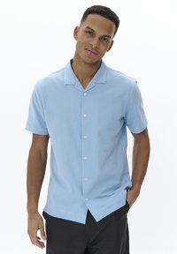 Camicia azzurra a maniche corte con colletto a camicia, texture liscia e cinque bottoni bianchi sul davanti.