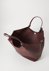 Bordeaux lærveske med glatt tekstur, åpen topp, to håndtak og trykknapp-lukking. Har minimalistisk design uten eksterne lommer.