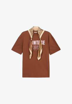 Bruine korte mouw t-shirt met "VINTAGE" print, gestyled met een gemêleerde beige en gouden sjaal die om de kraag is gedrapeerd.