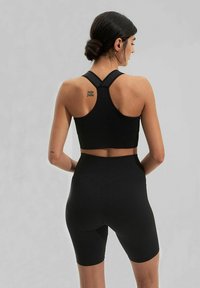 Černá mřížkovaná sportovní podprsenka s křížovým zadním designem, doplněná o vysoké mřížkované šortky. Hladká textura, přiléhavý střih, minimum detailů.