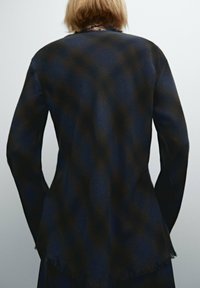 Dunkelblauer strukturiertes Jacke mit weichem Finish, mit einem leicht fransigen Saum und langen Ärmeln, von hinten betrachtet.