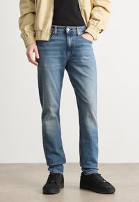 Ljusblå denimjeans med rak passform, lätt blekning framtill, fem fickor, knappstängning och stickade detaljer. Bärs med svarta sneakers.