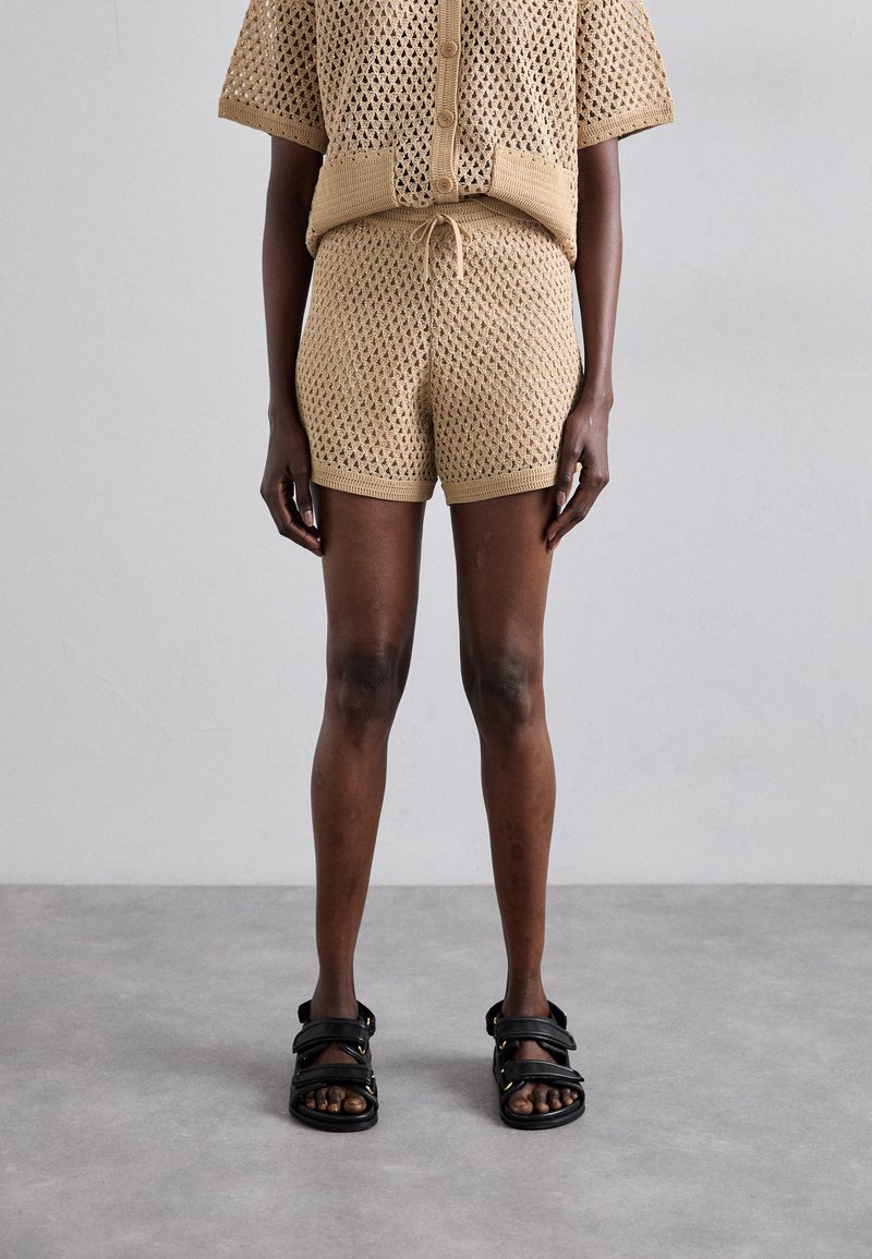 Beige crochet-knit two-piece set featuring a short-sleeve button-up top and matching shorts. Black sandals with multiple straps.
