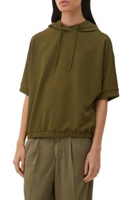 Sudadera corta de manga corta en verde oliva con un tejido texturizado, capucha con cordón y dobladillo inferior elástico. Combinada con pantalones sueltos en verde oliva.
