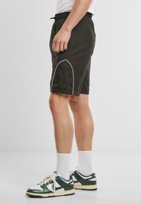 Shorts de sport noirs avec une taille à cordon, comprenant des accents de passepoil blancs et un tissu léger, portés avec des baskets vertes et blanches.
