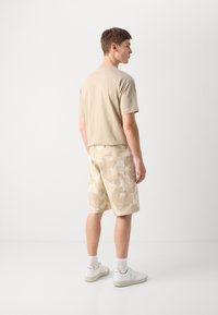 Beige cotton t-shirt and beige camouflage shorts. Casual fit, shirt with short sleeves, shorts have side pocket, paired with white sneakers.
