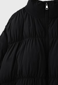 Doudoune noire avec col haut et fermeture éclair à l'avant, présentant des sections de tissu froncées et rembourrées pour l'isolation et le style.