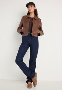 Veste courte en cuir marron avec col, associée à un jean denim bleu foncé taille haute. Baskets imprimé léopard beige et marron avec des lacets orange.