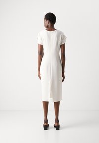 Abito midi bianco con maniche corte, tessuto testurizzato, design elegante, zip posteriore e uno spacco all'orlo. Sandali neri con tacco a blocco.