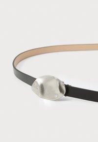 Zwarte leren riem met een dunne band en een gepolijste zilveren ovale gesp met een gegraveerd logo. Gladde textuur, minimalistisch ontwerp.