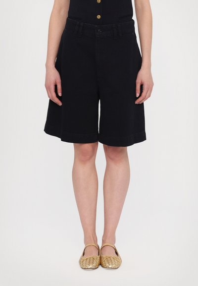 Shorts en coton noirs à coupe décontractée, longueur genoux, avec une fermeture à bouton classique et une taille, associés à des ballerines jaunes tissées.