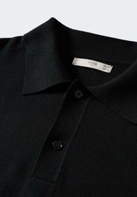 Polo noir en maille texturée, avec un col standard et deux boutons noirs au niveau du col. Étiquette visible à l'intérieur du col.