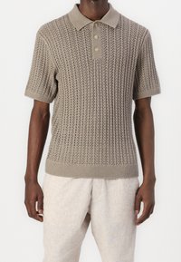 Knit polo skjorta i ljusbrun med korta ärmar, med en ribbad krage, knapplista och ett öppet mönster över hela plagget.