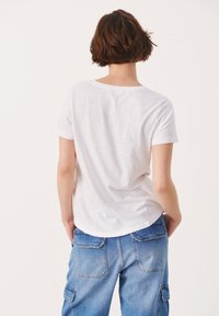 T-shirt bianco a maniche corte con scollatura rotonda, realizzato in tessuto leggero; indossato con pantaloni cargo blu in denim larghi, dotati di tasche.