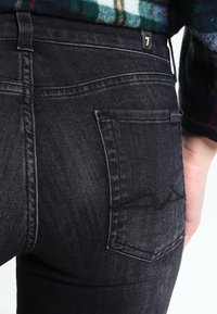 Czarne dżinsy z denimu o wąskim kroju. Posiadają tylną kieszeń z przeszytym wzorem oraz małą metkę z logo na pasku w talii.