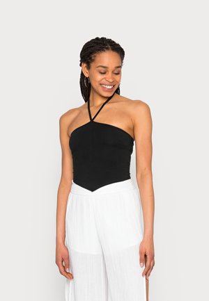 Top preto com decote halter e um design justo, combinado com calças brancas de perna larga em tecido texturizado.
