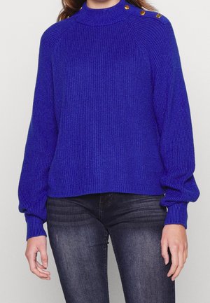 Pull en tricot bleu royal avec un col montant, texture côtelée et manches longues bouffantes. Présente des boutons dorés sur l'épaule.