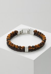 Bracciale in pelle e perline composto da perline di occhio di tigre marroni, pelle nera intrecciata e una chiusura in tono argento con dettagli del marchio.
