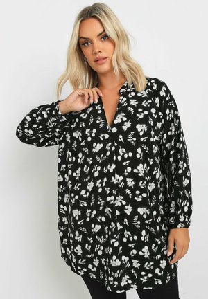 Blusa nera con stampa floreale bianca, maniche lunghe, scollatura a V, materiale fluido e vestibilità morbida. Presenta chiusura con bottoni e design a contrasto.