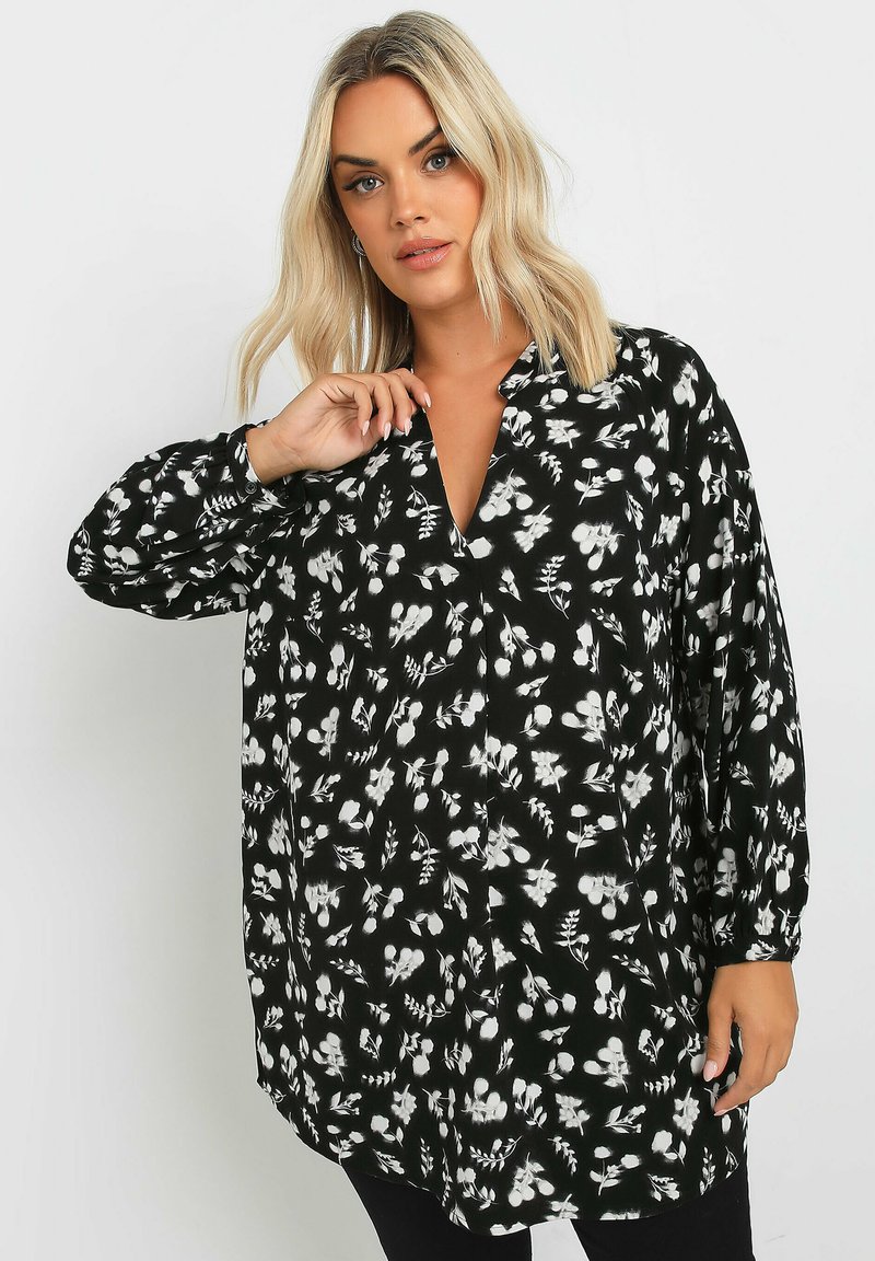 Blusa nera con stampa floreale bianca, maniche lunghe, scollatura a V, materiale fluido e vestibilità morbida. Presenta chiusura con bottoni e design a contrasto.