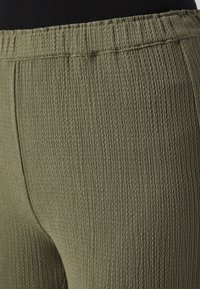 Olive green textured leggings with a ribbed pattern, featuring an elastic waistband for comfort. No visible seams along the sides.