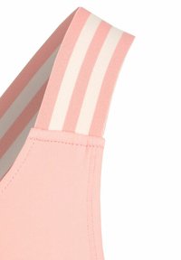 Lichtroze sportbh met een soepele textuur en een brede band met afwisselend roze en witte strepen. De stiksels zijn zichtbaar bij de naden.