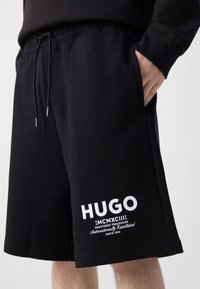Black shorts made from breathable fabric, featuring a drawstring waist, side pockets, and white printed branding on the hem.