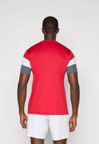 Camiseta atlética roja de mangas cortas, con acentos blancos y grises en los hombros. Fabricada con un tejido suave y ligero.