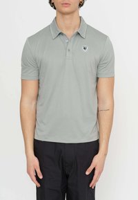Polo grigio con un collo classico, patta con tre bottoni e un piccolo logo nero e bianco sul lato sinistro del petto. Tessuto liscio.