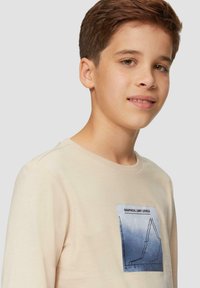 Beige Langarm-T-Shirt mit rundem Kragen, das auf der Vorderseite ein Grafikdesign eines Liniendiagramms in Blau und Schwarz zeigt.